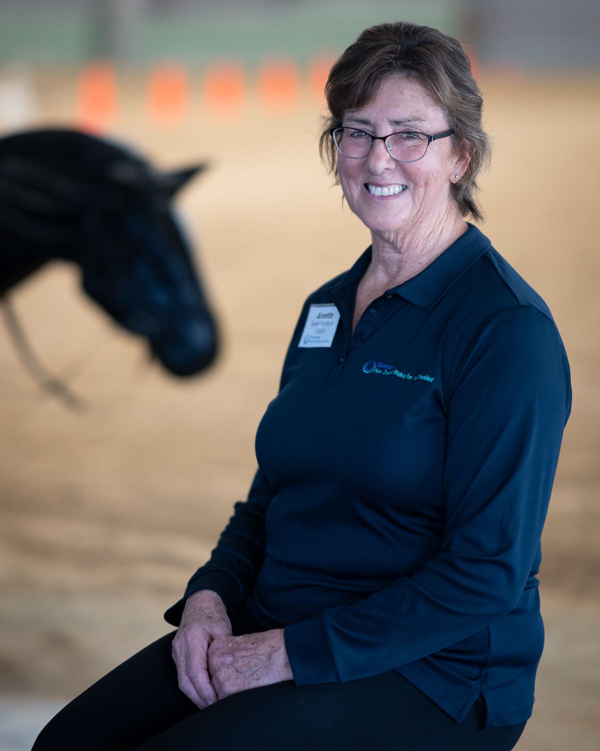 A smiling woman in a navy RDA polo shirt, seated in the arena