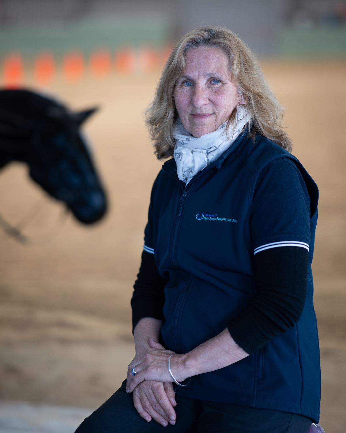 A woman with shoulder-length fair hair in a navy top, seated in the arena