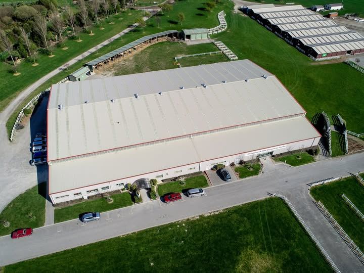 Aerial view of the large white indoor arena building surrounded by green paddocks