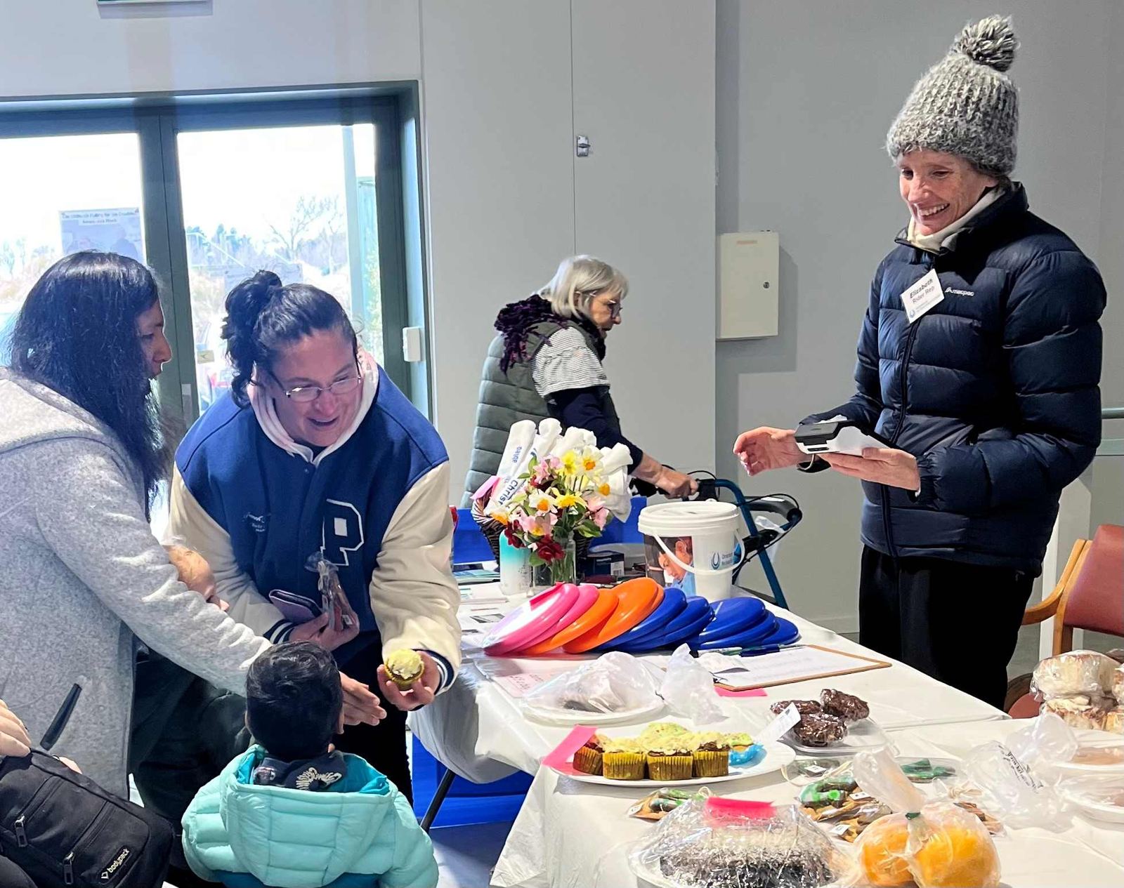 Volunteers and visitors around a table of baking at the fundraising stall