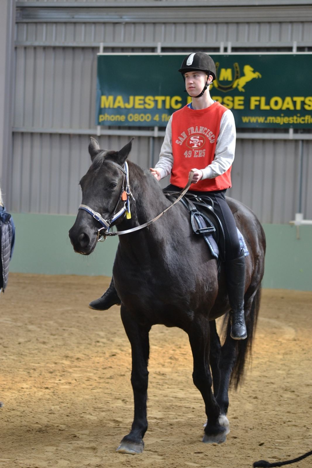 A rider in a red top on a dark horse during training in the arena