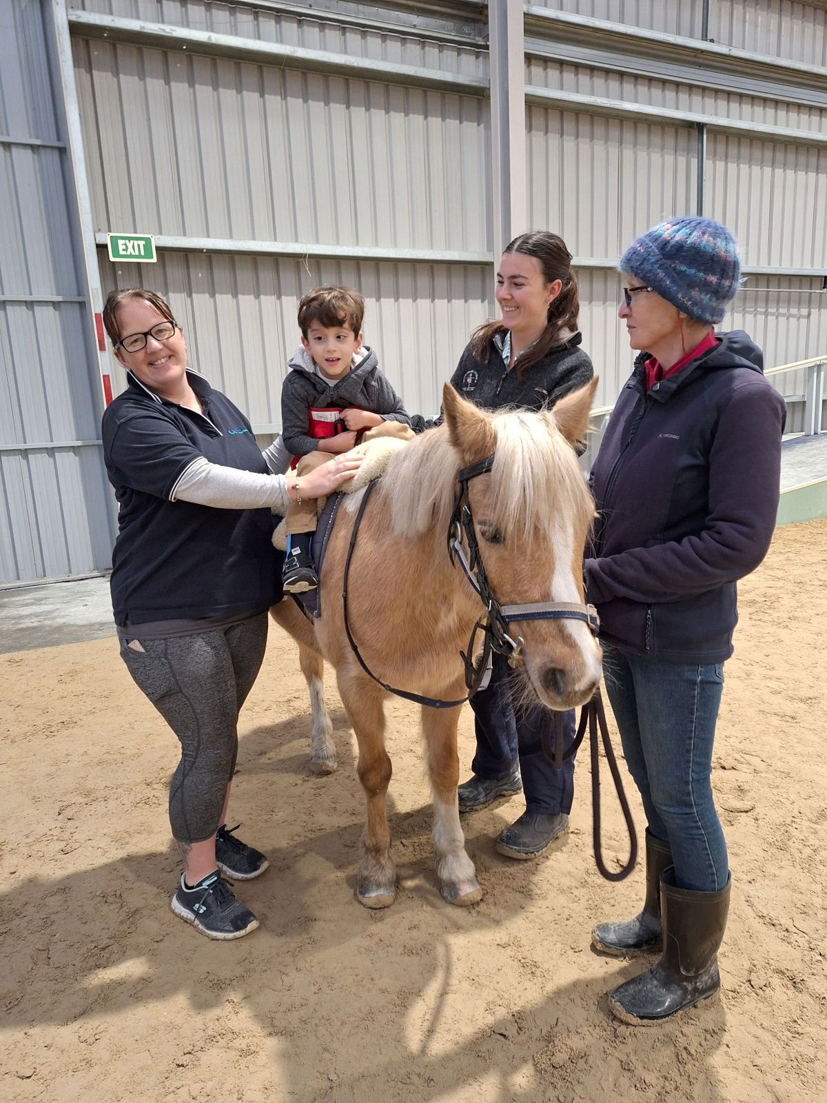 A young rider on Savvy the palomino, supported by three volunteers in the arena