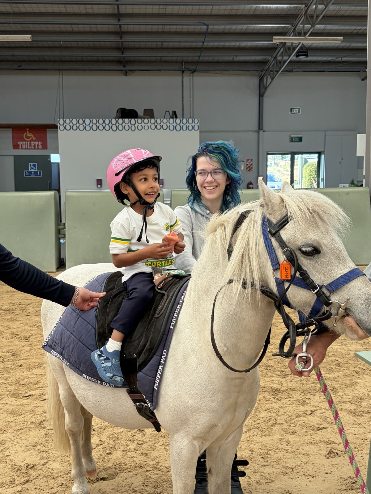 A volunteer leading a white pony with a young rider on board