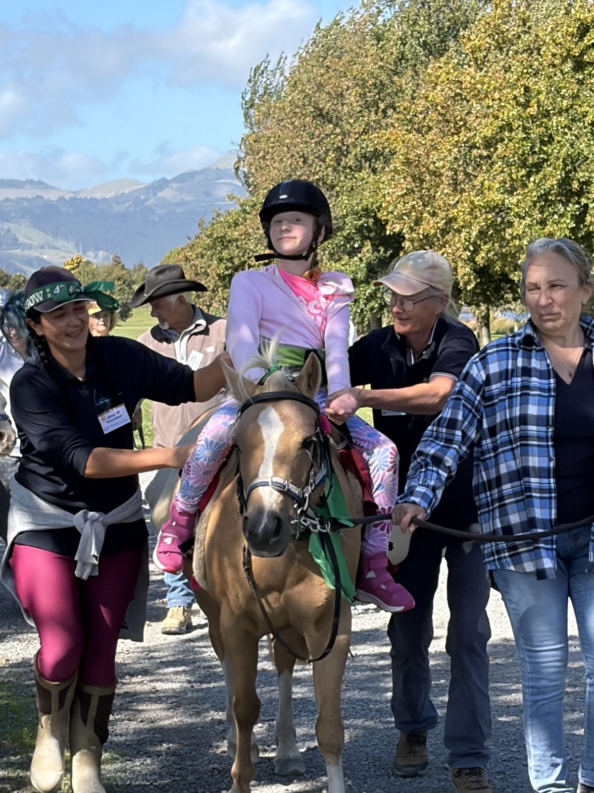Volunteers smiling beside a young rider on a pony outdoors